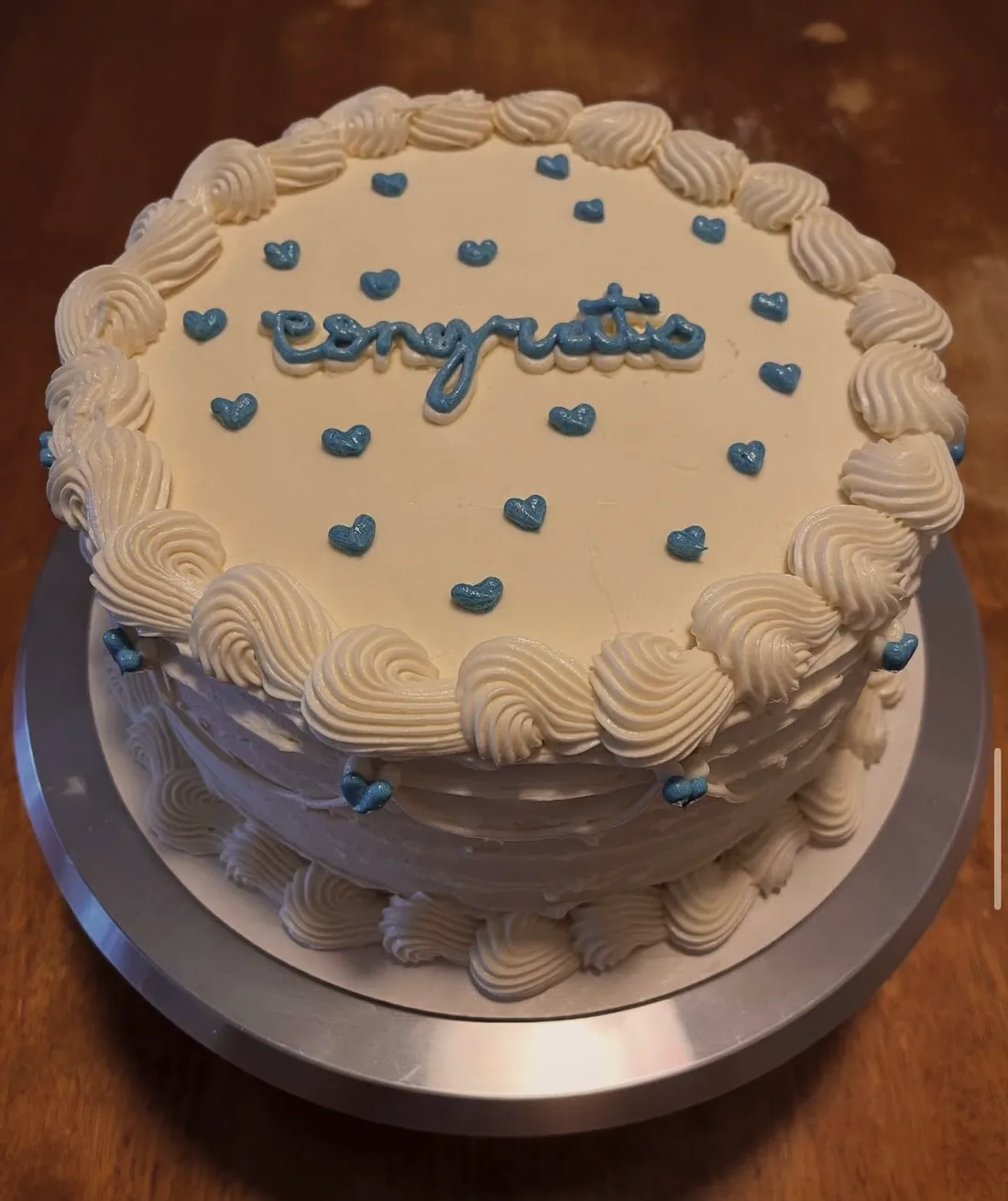 A white cake with blue piped hearts and hand-piped lettering
