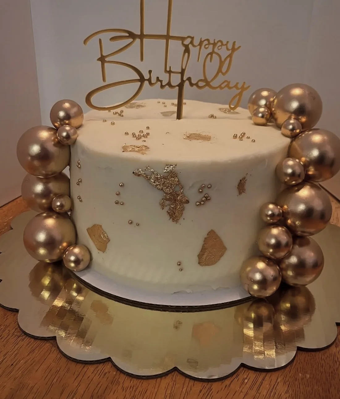 A white cake ringed with rose gold balloons and gold pearl work