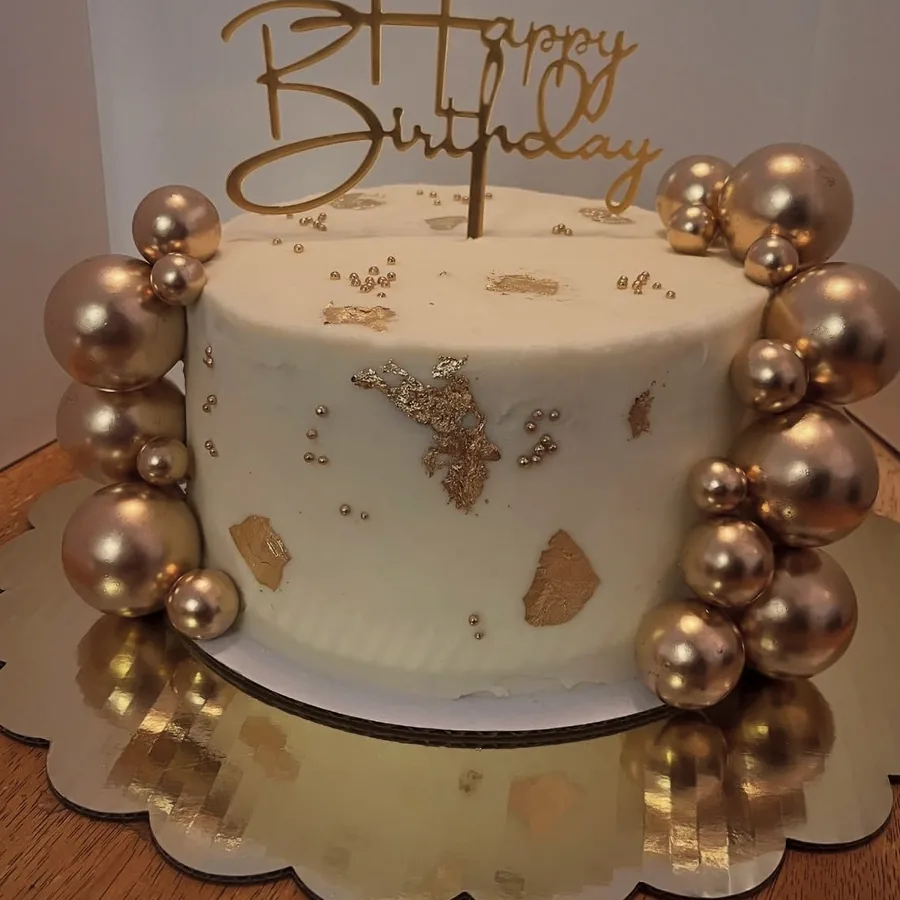 A white cake ringed with rose gold balloons and a gold Happy Birthday topper