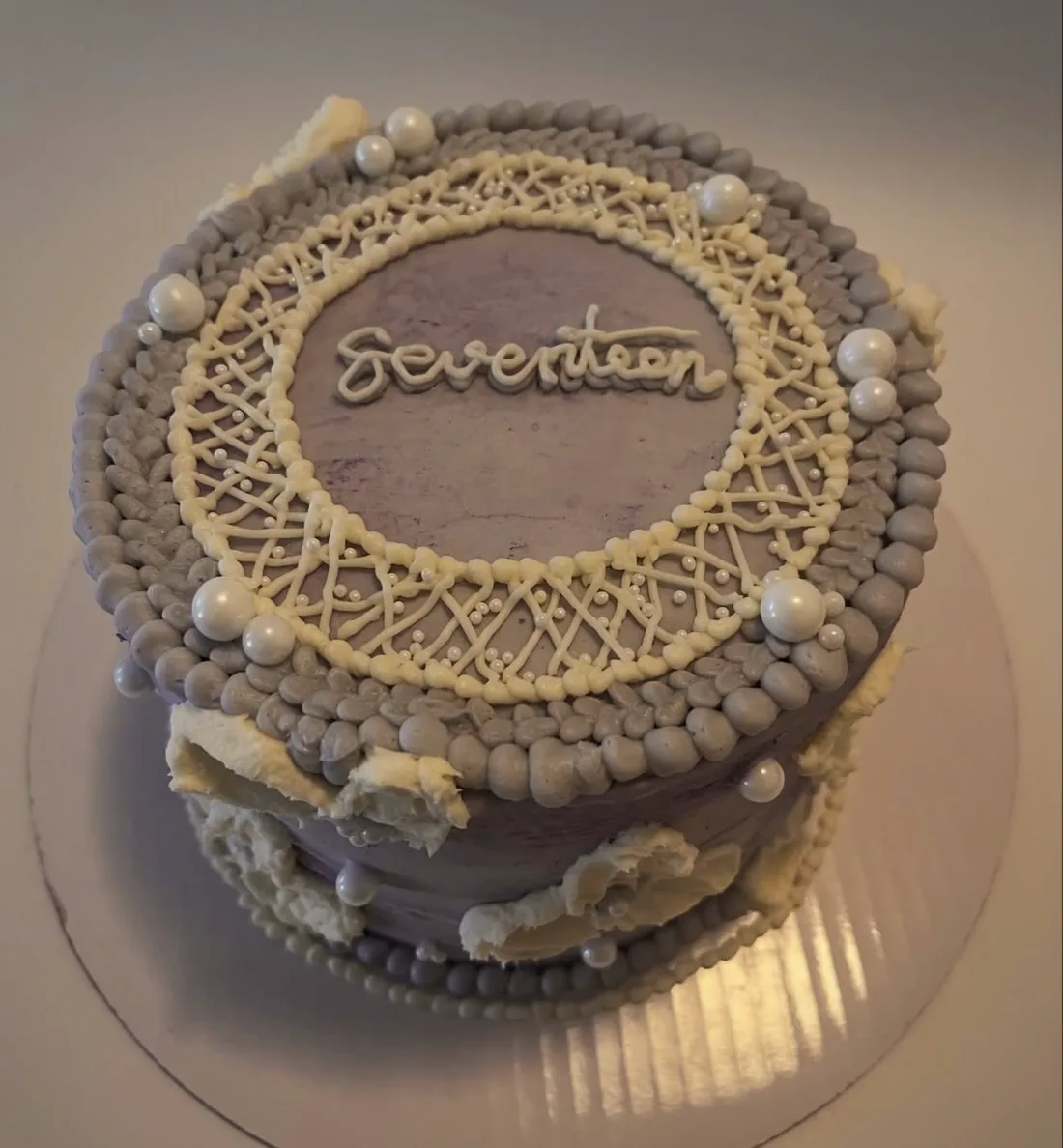 A lilac buttercream cake covered in fine white lace-style piping and silver pearls