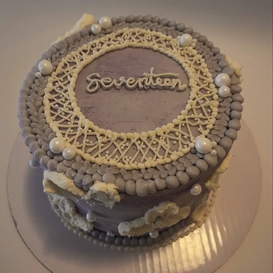 A lilac cake with white lace-style piping and silver pearls, lettered Seventeen