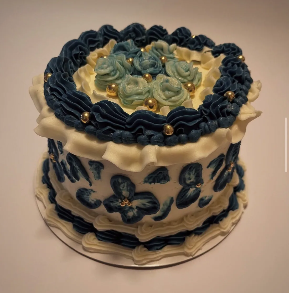 A navy and cream buttercream cake with piped roses and gold pearls on top