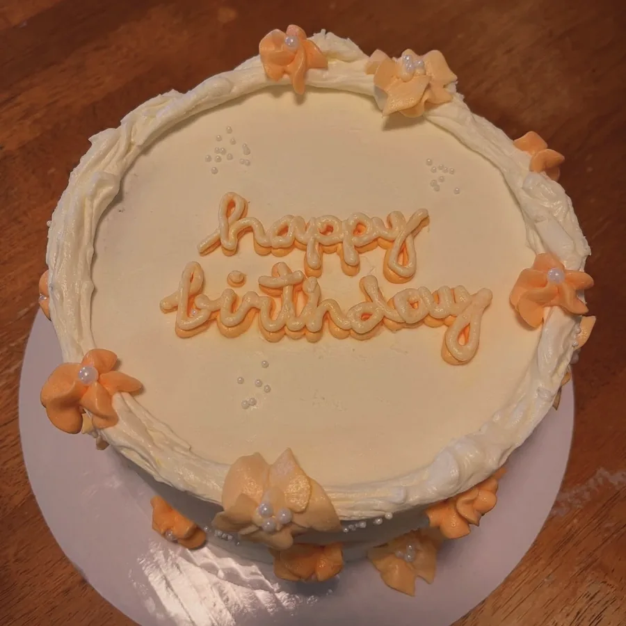 A cream cake with peach bows and hand-piped happy birthday lettering