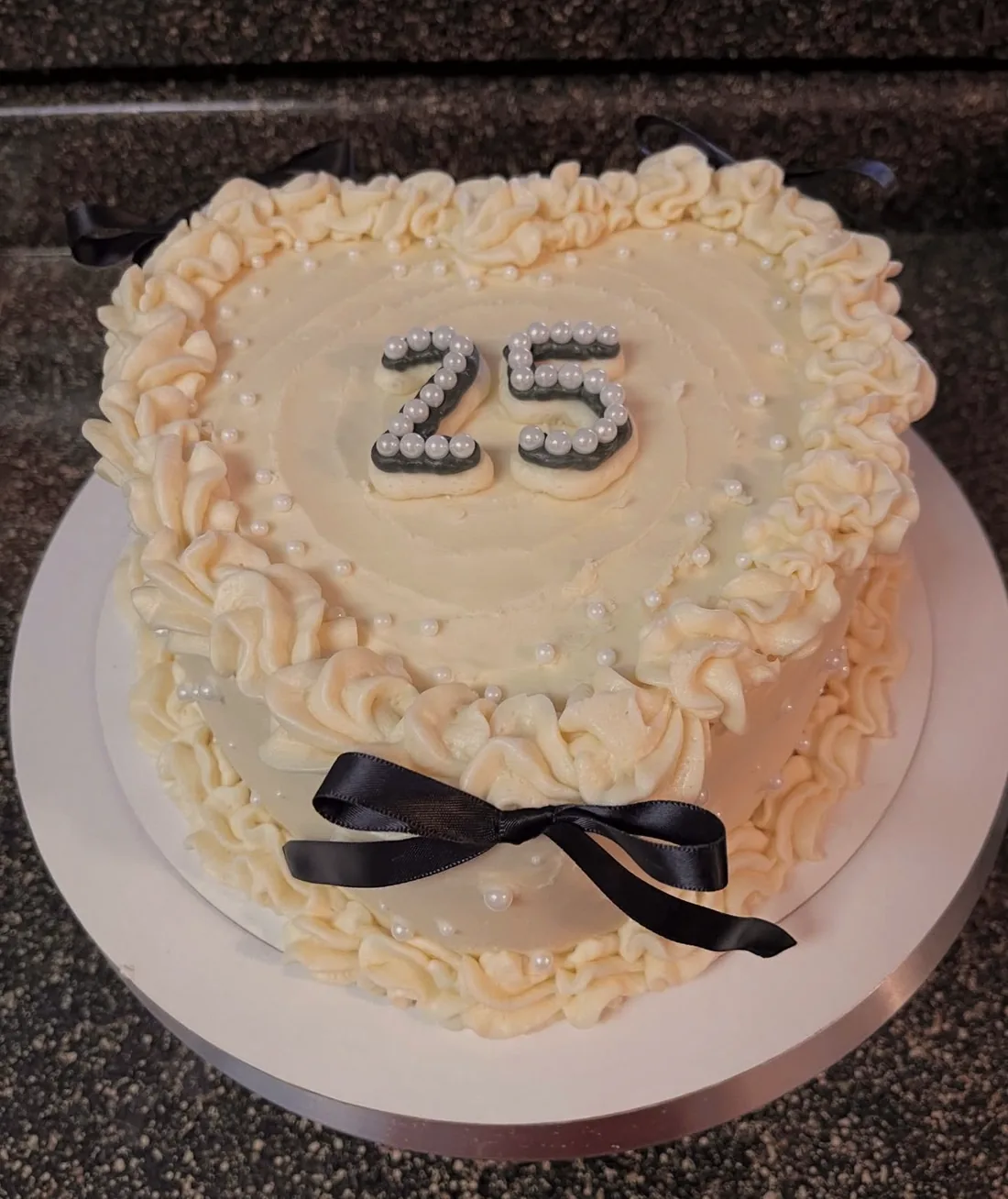 An ivory anniversary cake covered in hand-piped pearl work and tied with a black silk ribbon
