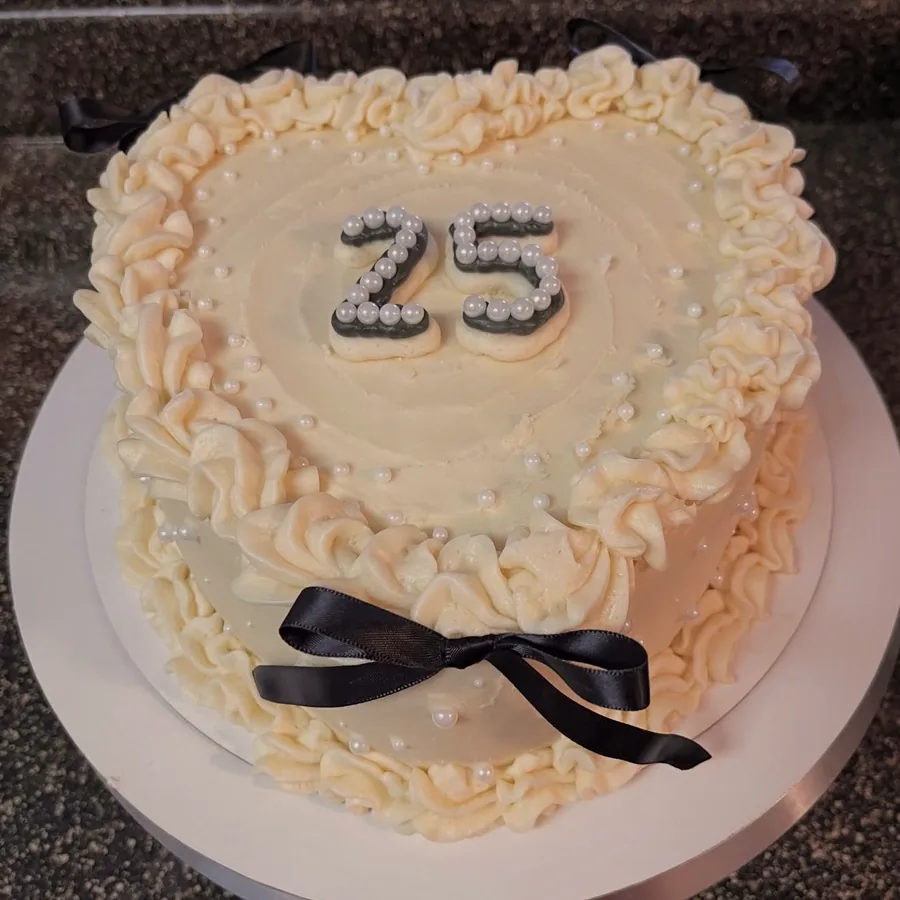 An ivory anniversary cake with pearl piping and a black silk ribbon, numbered 25