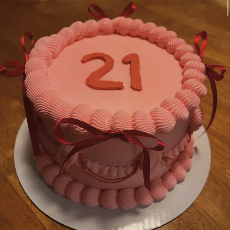 A pink buttercream cake with piped shell borders and a hand-piped twenty-first message