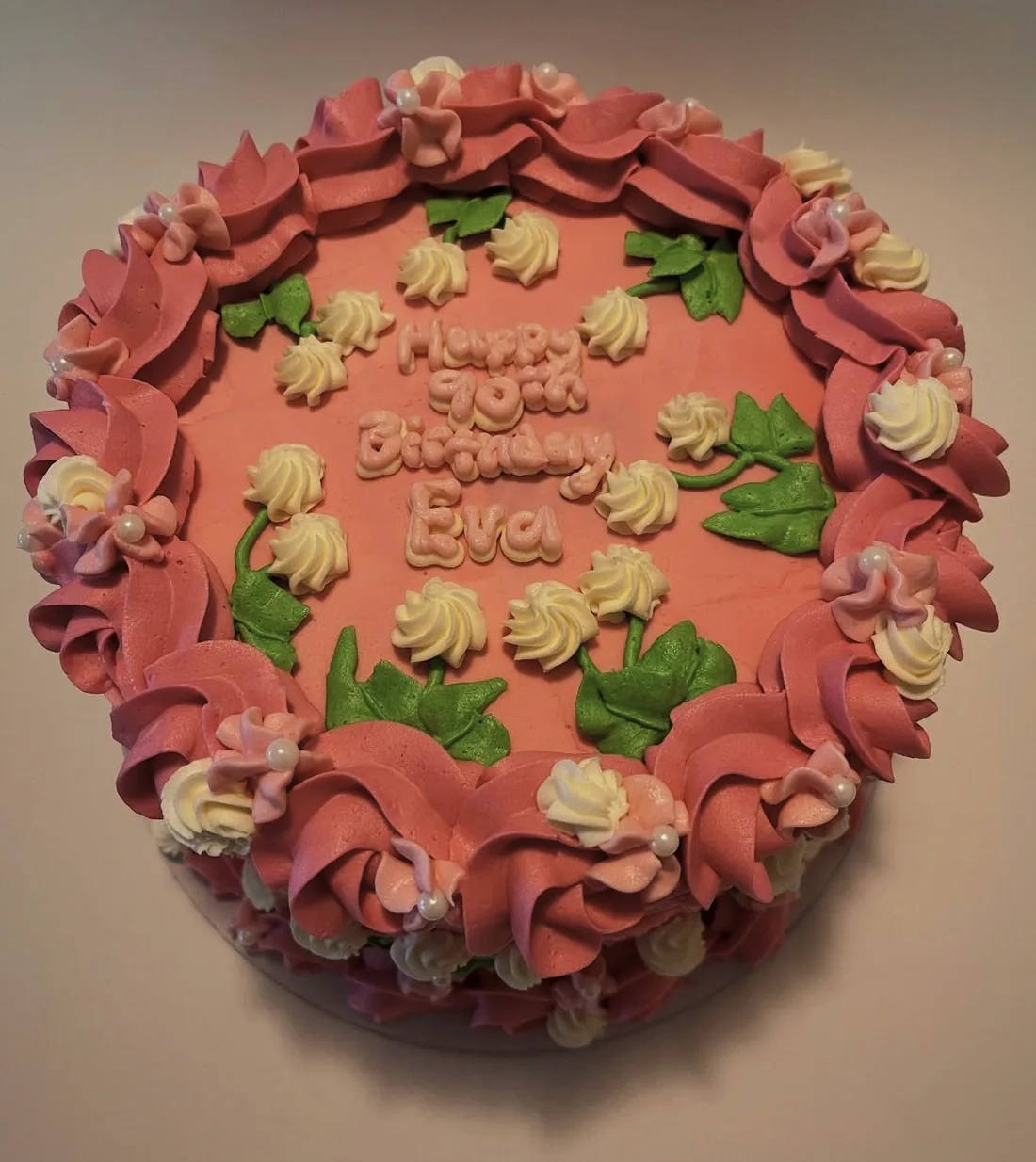 A dusty rose cake with piped buttercream ruffles, roses and green leaves