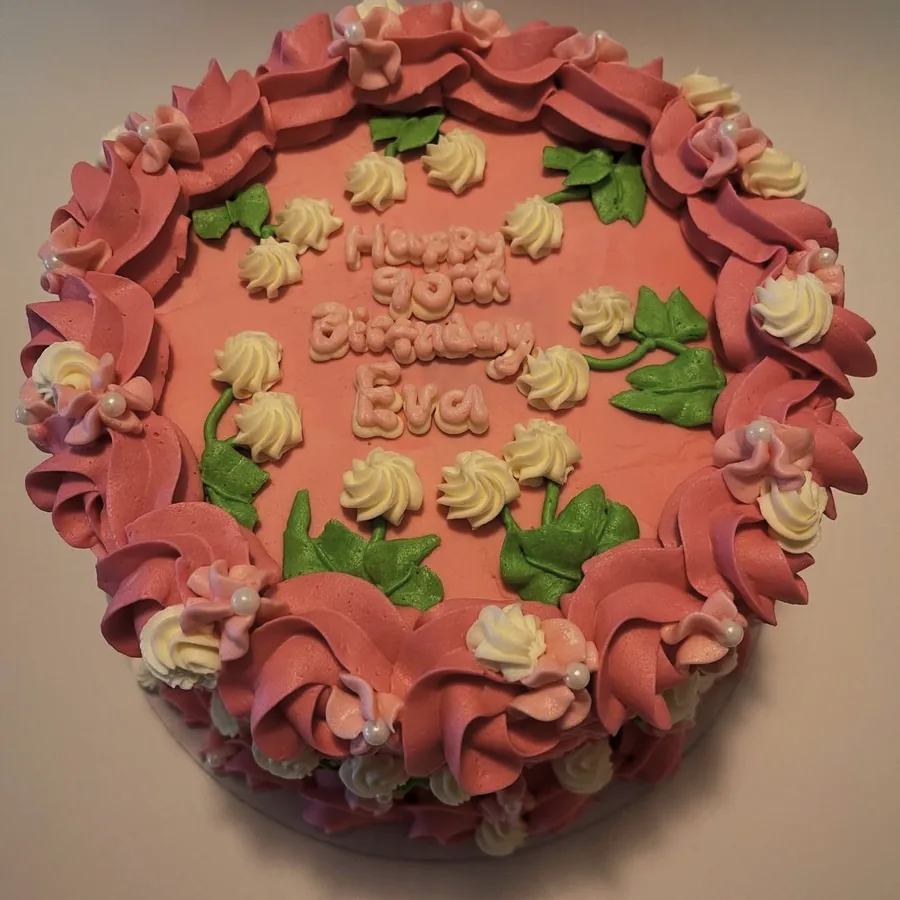 A dusty rose cake with piped ruffles, green leaves and a hand-piped birthday message