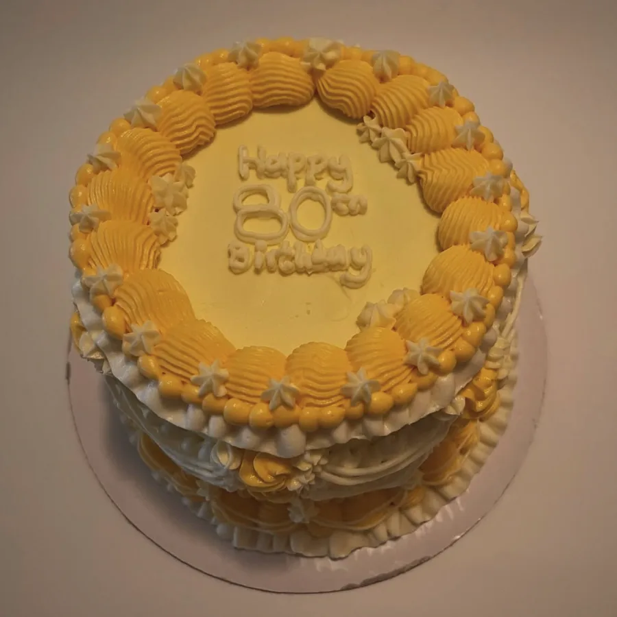 An eightieth birthday cake in butter yellow with a heavy piped shell border