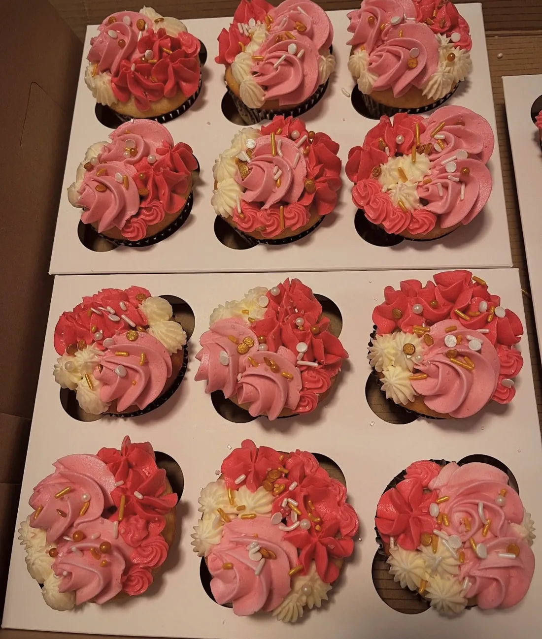 A box of a dozen cupcakes piped with pink and cream buttercream roses