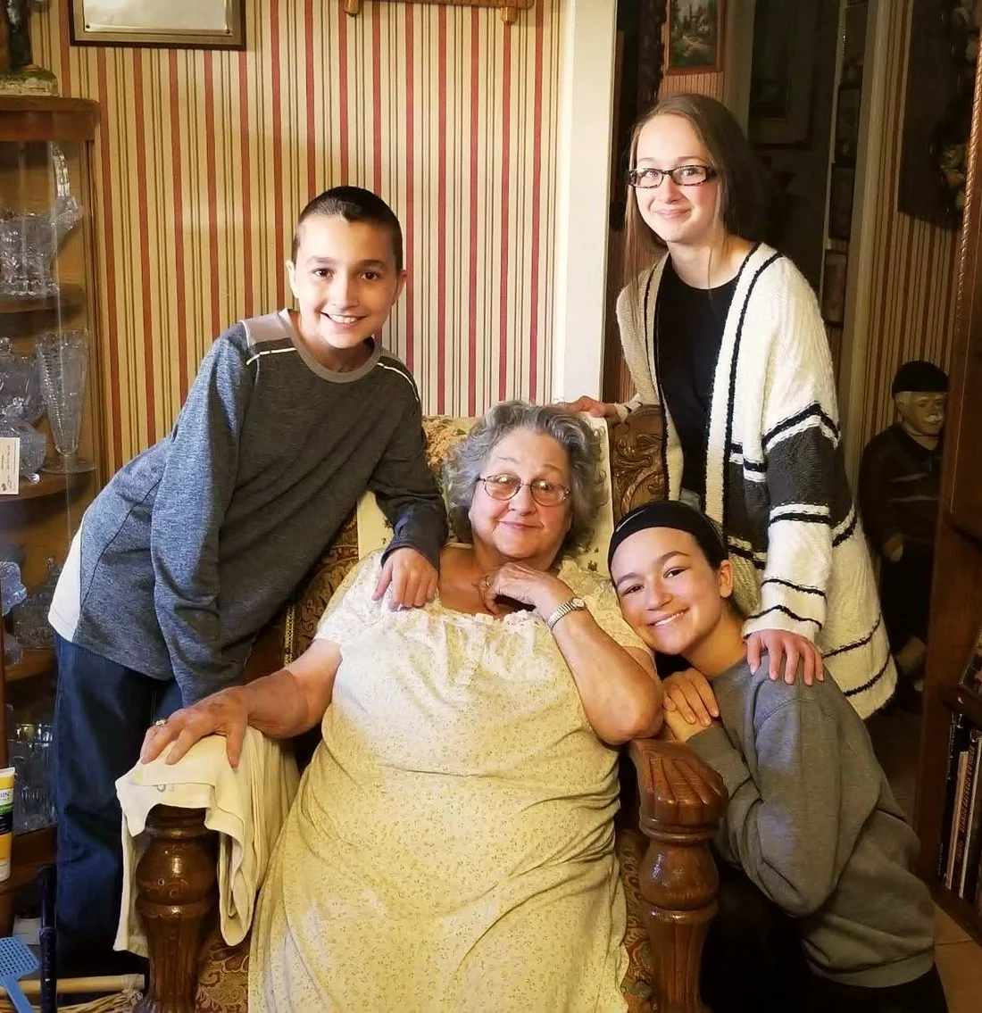 Mamaw Knipp sitting in her armchair at home with her three grandchildren gathered around her, all smiling