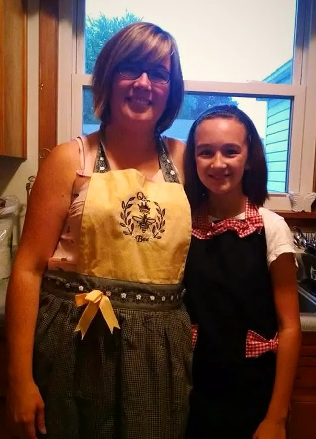 Ava as a young girl standing beside her mom, both wearing aprons in a home kitchen
